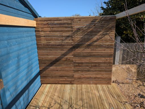 Completed horizontal slatted timber privacy screen alongside garden decking