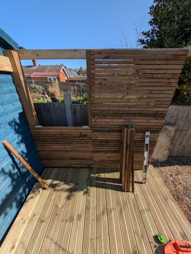 Horizontal timber slats being installed to create garden privacy screening beside decking